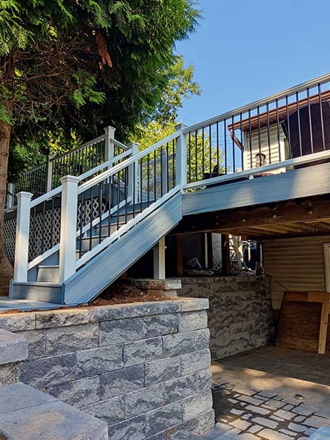 Renovated deck and patio area by True Built Construction featuring soft blue-gray composite decking, complemented by a robust white and black balustrade that encircles the space.