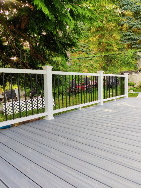True Built Construction's deck renovation displaying a chic, slate-grey composite deck flooring that seamlessly blends with classic white railings. The spacious deck is encased in lush greenery, providing a serene outdoor living space with a contemporary feel