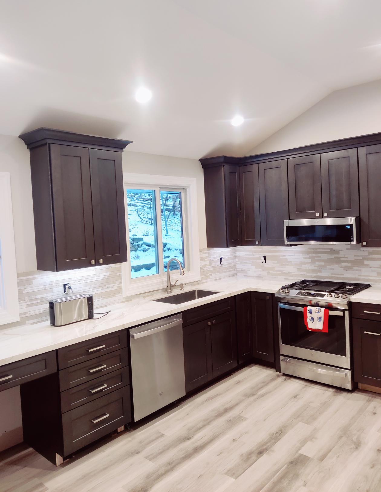 A sophisticated kitchen remodel boasting dark wooden cabinets and stainless steel appliances, completed by True Built Construction. The elegant design is highlighted by white marble countertops and a linear tile backsplash, creating a luxurious and functional cooking space