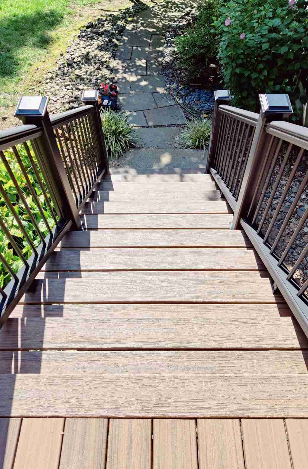 Artfully crafted deck stairs by True Built Construction with richly stained wooden planks leading down to a charming garden path. The railings are adorned with high-quality, black aluminum balusters.
