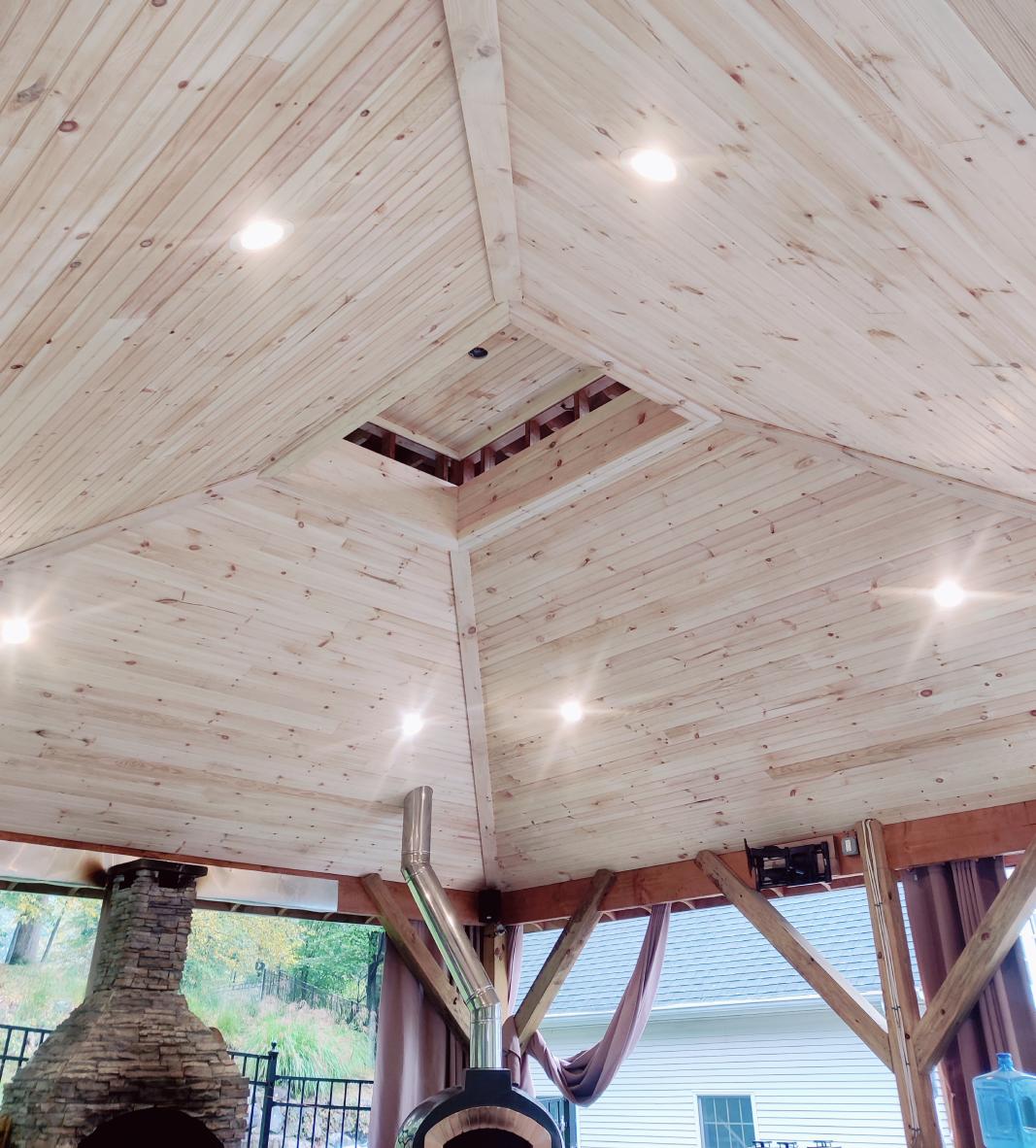True Built Construction's recent project, an open-air wooden gazebo with a stunning vaulted ceiling, showcasing natural pine boards and recessed lighting. The craftsmanship accentuates the inviting ambiance of this outdoor entertainment area.